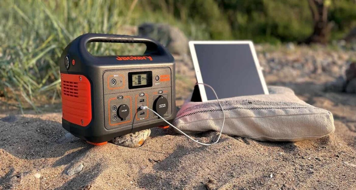 Jackery Générateur solaire 500 rechargeant une tablette sur une plage de sable, avec de la végétation en arrière-plan