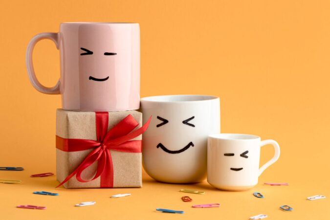 Collection de mug humoristique avec visages expressifs souriants et clins d'œil sur fond orange festif avec cadeau