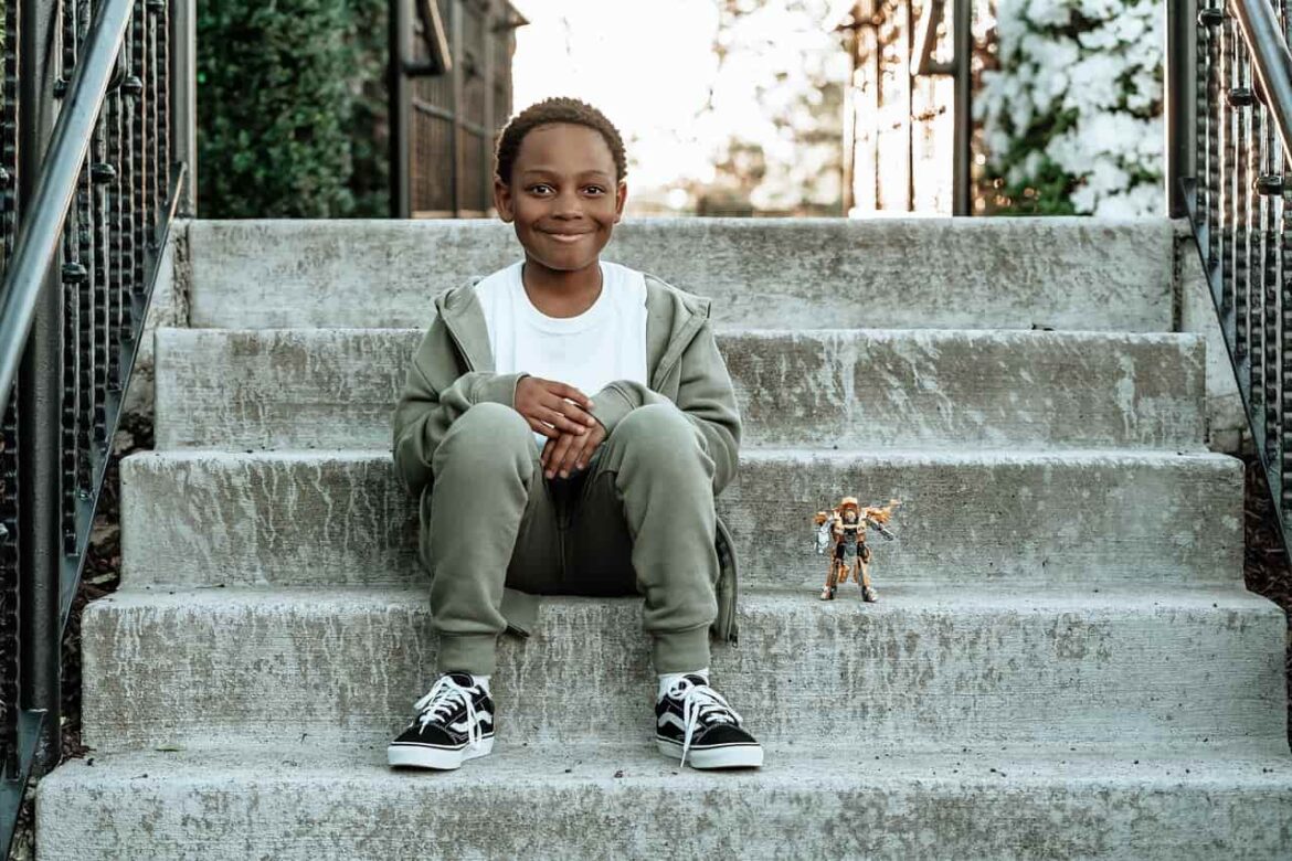 Un jeune garçon souriant est assis sur des escaliers en béton avec une figurine, illustrant l'importance de la sécurité et des "Localisateurs GPS Enfants".