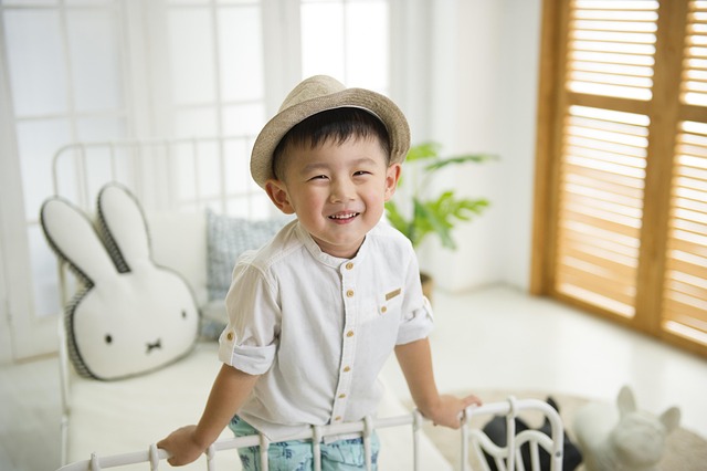 Un jeune enfant asiatique souriant portant un chapeau, avec des traceurs GPS pour enfants en arrière-plan pour la sécurité.