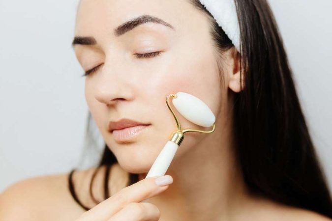 Une jeune femme utilise des rouleaux de jade sur son visage pour un soin de la peau relaxant.