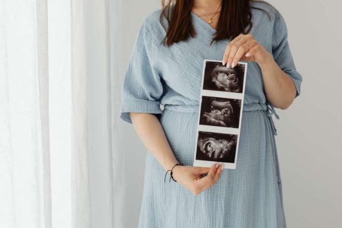 Une femme enceinte, portant une robe bleue, tient délicatement des échographies, anticipant avec joie l'arrivée de son premier bébé.