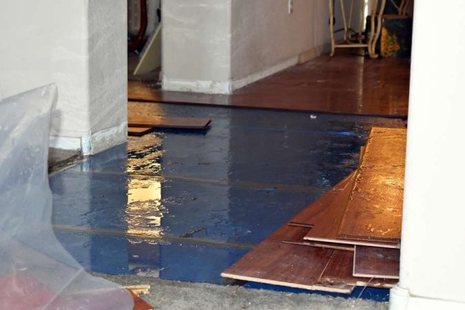 Un sol inondé d'eau bleu sous un plancher en bois démonté, près de murs en plâtre.